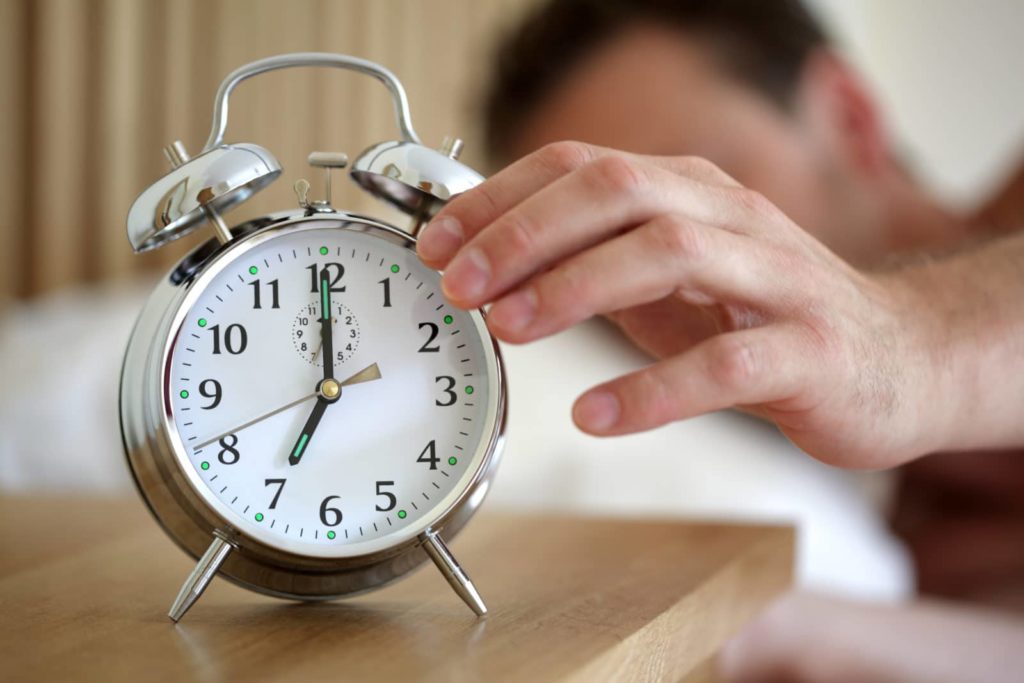 a man's hand reaching for an alarm clock