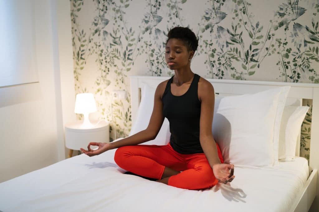 Young black woman doing meditation exercises on her bed at home