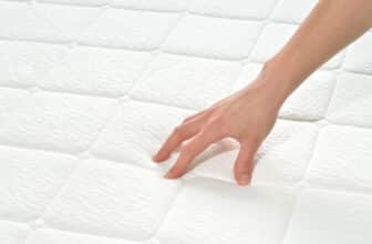 A person's hand is touching a sagging mattress.